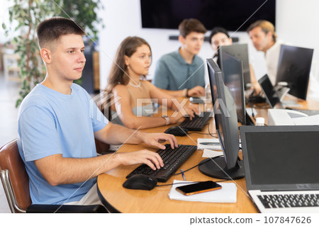 Focused guy studying in computer lab with fellow students 107847626