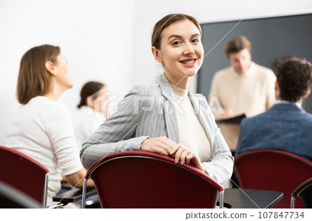 Cheerful woman turning around and looking at camera during advanced training course in auditorium Cheerful woman turning around and looking at camera during advanced training course in auditorium 107847734