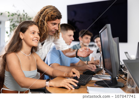 During computer lesson, male teacher helps girl student complete difficult task, 107847741