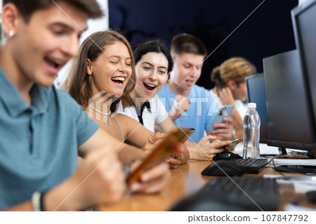 At computer class, young girl student sits with mobile phone and listens admiringly to teacher 107847792