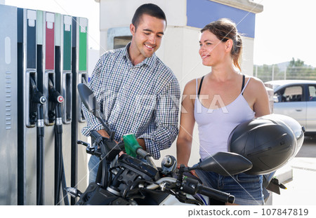 Smiling man and woman filling motor-cycle with gasoline 107847819