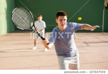 Young male pelota player hitting ball with racket 107847939