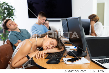 Exhausted young female student sleeping at table in computer classroom Exhausted young female student sleeping at table in computer classroom 107847978