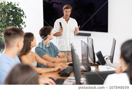 Adult man speaker stands in front of students and talks about use of artificial intelligence 107848039