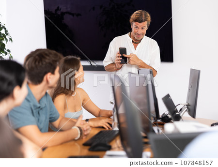 Positive teacher recommending educational mobile app to group of students Positive teacher recommending educational mobile app to group of students 107848157