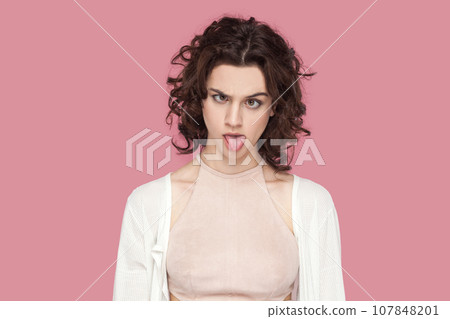 Portrait of crazy fool woman with curly hair wearing casual style outfit having foolish facial expression, grimacing, showing bad manners. Indoor studio shot isolated on pink background. 107848201