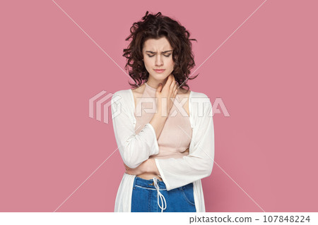 Portrait of sad upset unhappy woman with curly hair wearing casual style outfit standing looking down, crying, hearing bad news. Indoor studio shot isolated on pink background. 107848224