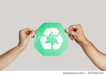 Closeup of woman and man hand holding green recycling sign, ecological icon, environment protection. Indoor studio shot isolated on gray background. 107848245