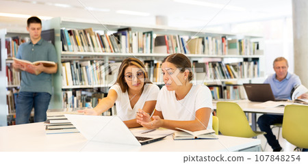 Student girls work together on project in the college library Student girls work together on project in the college library 107848254