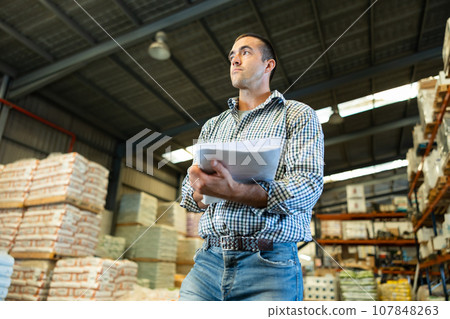 Man standing in warehouse and verifying documents with presence of goods in the warehouse of industrial goods 107848263
