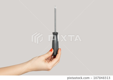 Closeup of woman hand showing black metal and plastic tool screwdriver for repair. Indoor studio shot isolated on gray background. 107848313