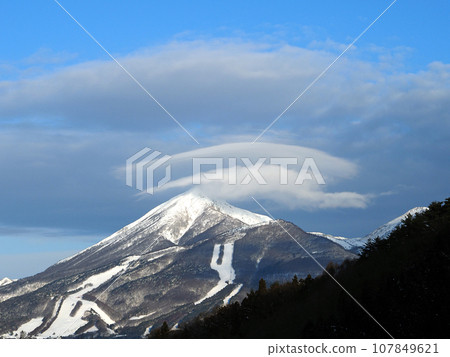 The double umbrella clouds that hang over the snow-capped Mt. Bandai are covered with another layer of clouds, making for an impressive and beautiful sight against the blue sky. 107849621