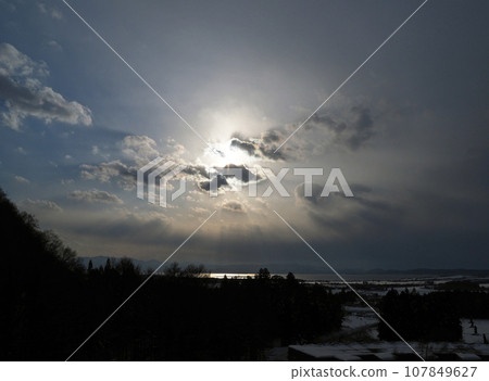 The sun hidden behind the clouds above Lake Inawashiro. The light from there makes the surface of the lake shine white, making it look impressive and beautiful against the snowy landscape. 107849627