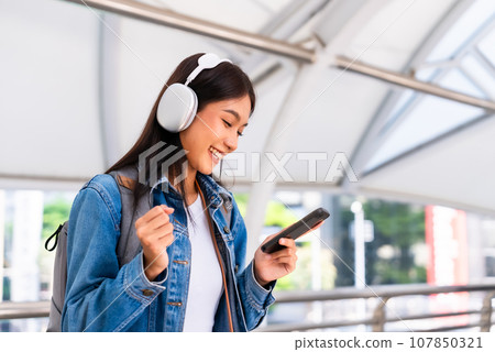 Portrait of happy young asian woman listening music online with wireless headphones 107850321