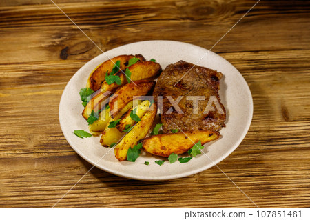 Fried beef steak with potato wedges on wooden table Fried beef steak with potato wedges on wooden table 107851481