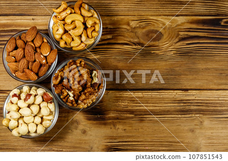 Assortment of nuts on wooden table. Almond, hazelnut, walnut and cashew in glass bowls. Top view, copy space. Healthy eating concept Assortment of nuts on wooden table. Almond, hazelnut, walnut and cashew in glass bowls. Top view, copy space. Healthy eating concept 107851543