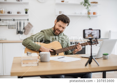 Inspired man playing guitar while recording video on mobile 107851600