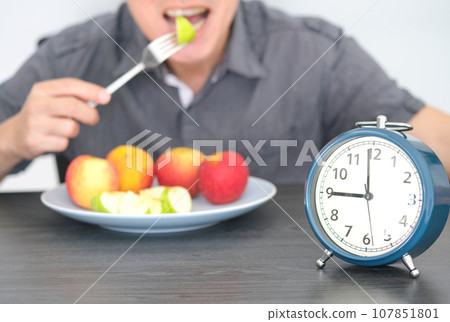 Ancient clock . Black ground young man eating fruit, fiber and dietary fiber. healthy food concept Ancient clock . Black ground young man eating fruit, fiber and dietary fiber. healthy food concept 107851801