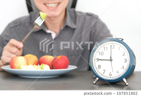 Ancient clock . Black ground young man eating fruit, fiber and dietary fiber. healthy food concept Ancient clock . Black ground young man eating fruit, fiber and dietary fiber. healthy food concept 107851802
