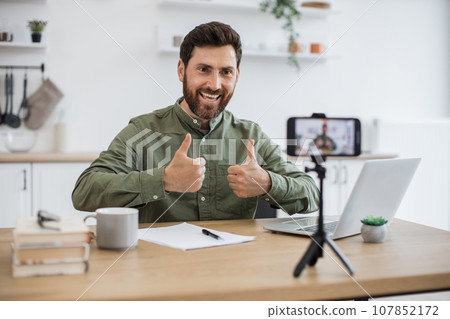 Man working on laptop and recording video on smartphone 107852172