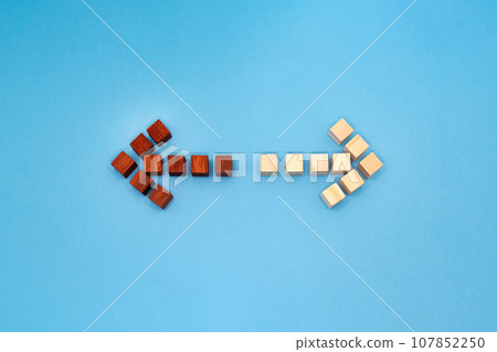 Front view of red and yellow wood cube arrows pointing in opposite directions on blue background Front view of red and yellow wood cube arrows pointing in opposite directions on blue background 107852250