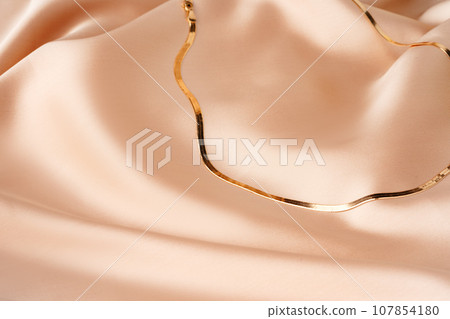 Golden chain necklace on beige silk background 107854180