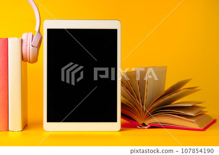 Books with digital tablet and headphones on yellow background Books with digital tablet and headphones on yellow background 107854190