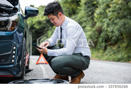 Portrait man sitting while calling roadside assistance after breaking down. Elegant middle age businessman wearing white shirt and waiting for help car accident on road. Roadside assistance concept. Portrait man sitting while calling roadside assistance after breaking down. Elegant middle age businessman wearing white shirt and waiting for help car accident on road. Roadside assistance concept. 107856266