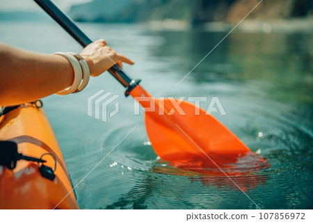 Kayak paddle sea vacation. Person paddles with orange paddle oar on kayak in sea. Leisure active lifestyle recreation activity rest tourism travel Kayak paddle sea vacation. Person paddles with orange paddle oar on kayak in sea. Leisure active lifestyle recreation activity rest tourism travel 107856972