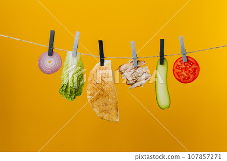 Doner kebab with ingredients hanging on a thread in the air : beef meat, lettuce, onion, tomatoes, cheese, cucumber. Yellow background Doner kebab with ingredients hanging on a thread in the air : beef meat, lettuce, onion, tomatoes, cheese, cucumber. Yellow background 107857271