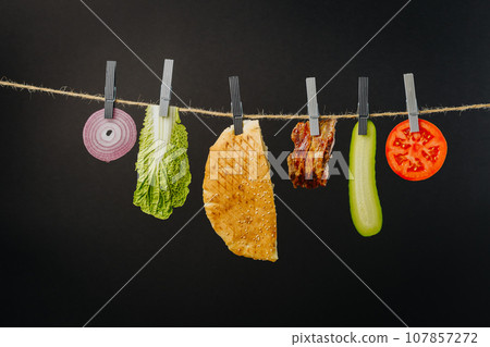 Doner kebab with ingredients hanging on a thread in the air : beef meat, lettuce, onion, tomatoes, cheese, cucumber. Black background 107857272