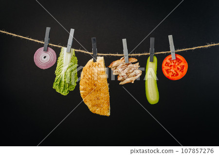 Doner kebab with ingredients hanging on a thread in the air : beef meat, lettuce, onion, tomatoes, cheese, cucumber. Black background Doner kebab with ingredients hanging on a thread in the air : beef meat, lettuce, onion, tomatoes, cheese, cucumber. Black background 107857276