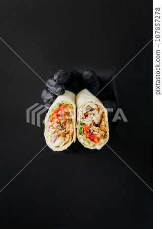 Hands holding doner or shawarma through torn holes in black paper background. Street food concept Hands holding doner or shawarma through torn holes in black paper background. Street food concept 107857278