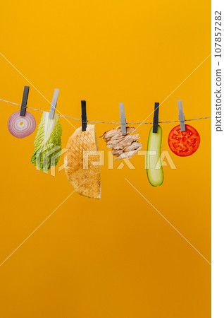 Doner kebab with ingredients hanging on a thread in the air : beef meat, lettuce, onion, tomatoes, cheese, cucumber. Yellow background Doner kebab with ingredients hanging on a thread in the air : beef meat, lettuce, onion, tomatoes, cheese, cucumber. Yellow background 107857282