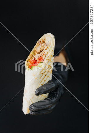 Hand holding doner or shawarma through torn holes in black paper background. Street food concept Hand holding doner or shawarma through torn holes in black paper background. Street food concept 107857284