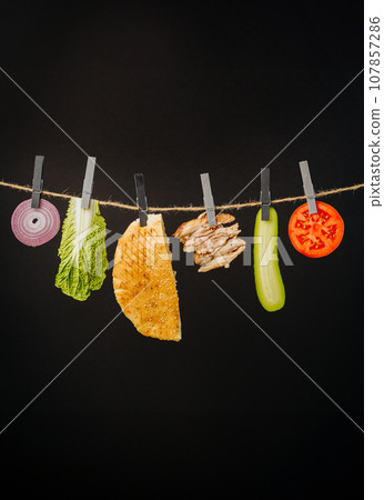 Doner kebab with ingredients hanging on a thread in the air : beef meat, lettuce, onion, tomatoes, cheese, cucumber. Black background 107857286