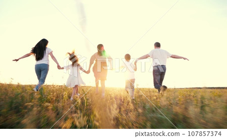 Happy family with little children runs joining hands across green rural meadow 107857374