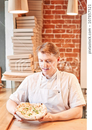 The chef holds a pizza in his hands. Neapolitan pizza from a wood-fired oven. Pizza is on the plate. Pizza with pear and gorgonzola. Fast delivery of food.  107857521