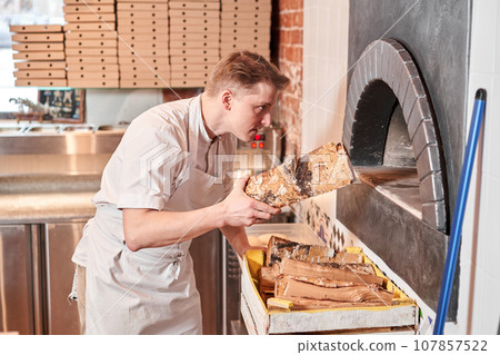 The chef prepares pizza in a neapolitan pizzeria. Cook in a apron in the kitchen with a shovel in his hands. boxes for food delivery on background. 107857522
