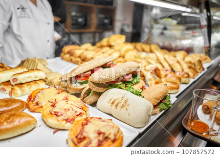 Fresh sandwiches, pies and pizza to choose from in the window of a cafe, buffet or self-service cafe. Croissant with ham and cheese. Hot pastries lie on the shelf in the cafe. Buns in the store. Fresh sandwiches, pies and pizza to choose from in the window of a cafe, buffet or self-service cafe. Croissant with ham and cheese. Hot pastries lie on the shelf in the cafe. Buns in the store. 107857572