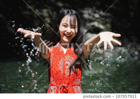 A woman wearing a red dress standing in a mountain stream A woman wearing a red dress standing in a mountain stream 107857911