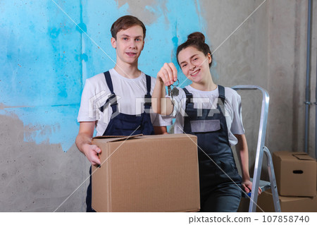 Own home. Mortgage relocation concept. Happy couple holding key from new first house. Family celebrating moving day. Husband wife customers buyers purchase real estate hold moving box showing keys 107858740