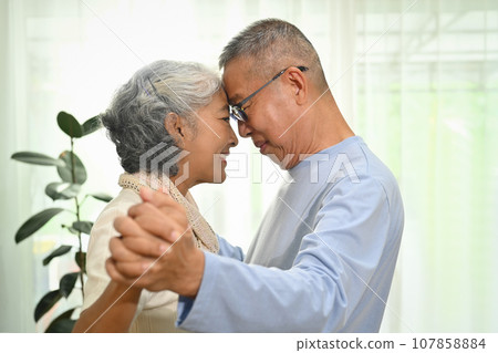 Happy elderly couple spouses dancing in living room while spending time together at home 107858884