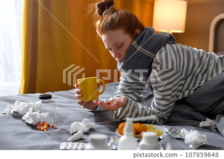 redhead lady with cold blowing runny nose and swollen throat sitting on bed at home redhead lady with cold blowing runny nose and swollen throat sitting on bed at home 107859648