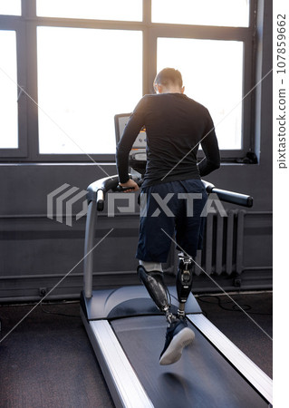 back shot of man with artificial legs running on treadmills at gym back shot of man with artificial legs running on treadmills at gym 107859662