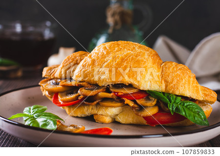 Close up of fresh croissant with fried mushrooms, tomatoes and basil on a plate Close up of fresh croissant with fried mushrooms, tomatoes and basil on a plate 107859833