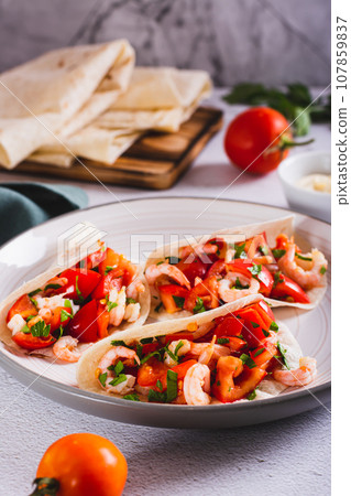 Vegetarian mini tacos with tomatoes, shrimp and herbs on a plate on the table vertical view 107859837