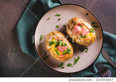 Close up of baked whole potatoes with egg, sausages and herbs on a plate top view Close up of baked whole potatoes with egg, sausages and herbs on a plate top view 107859847
