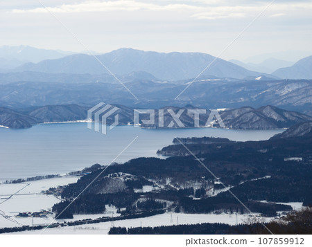 A large lake surrounded by snowy mountains and fields (Fukushima Prefecture, Inawashiro Town) 107859912