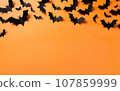 Halloween decorations, bats on vibrant orange background. Happy holiday concept. Party greeting card mockup with copy space at the bottom. Flat lay, overhead, top view 107859999